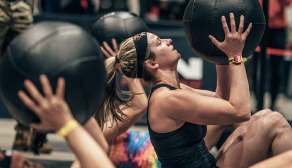 Woman doing a sit up with a medicine ball in a DEKA Strong Competition